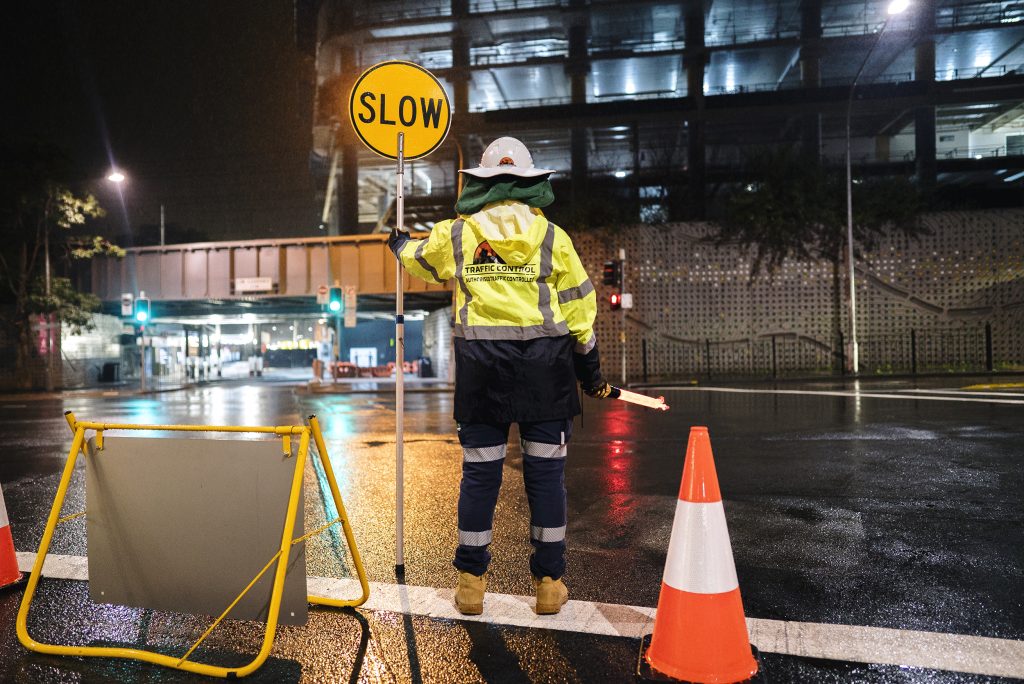 An SSTC traffic controller standing on a wet road holding a slow sign.