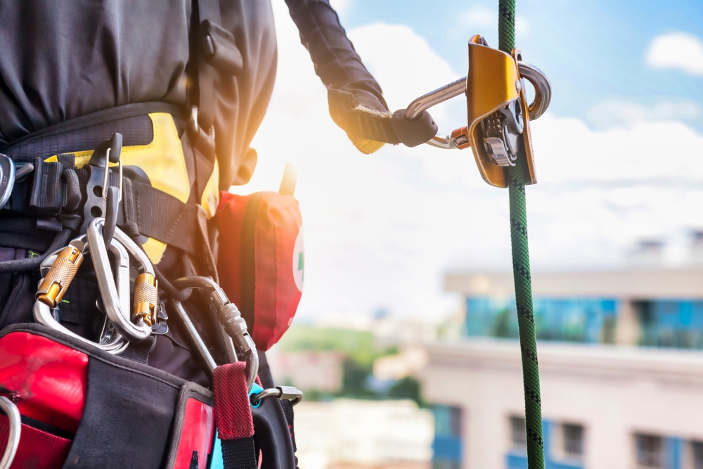 The back of a construction worker working at heights clipped to a safety rope.