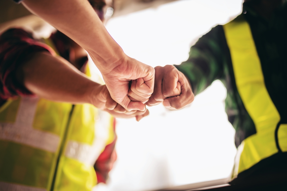 Three construction workers fist bumping in a circle.