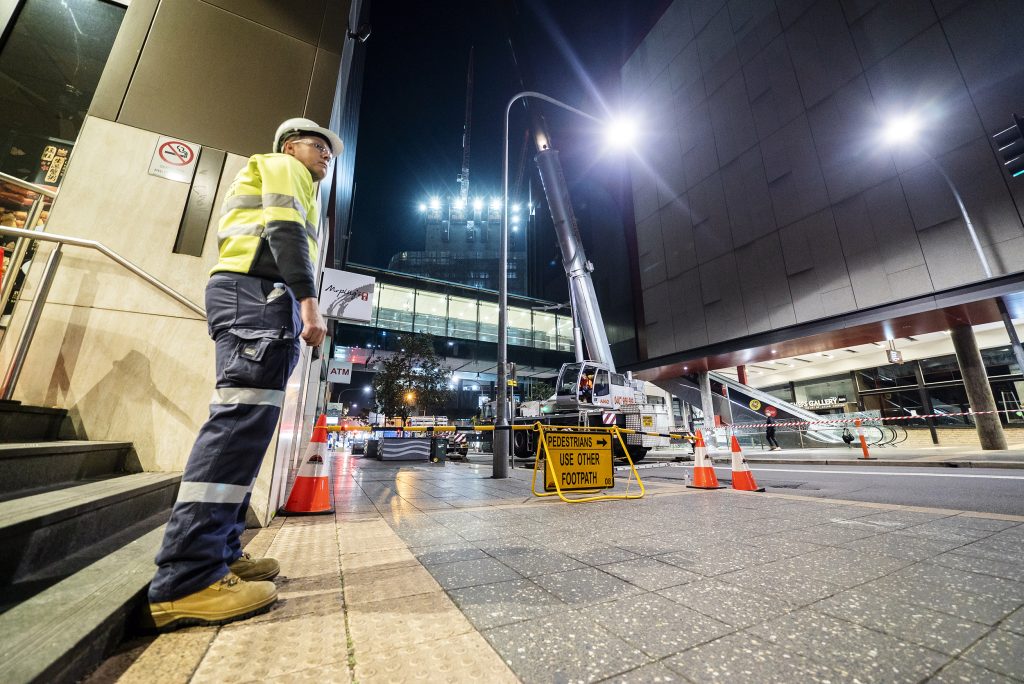 An SSTC traffic controller standing on a footpath before a road closed sign directing pedestrians and traffic. 