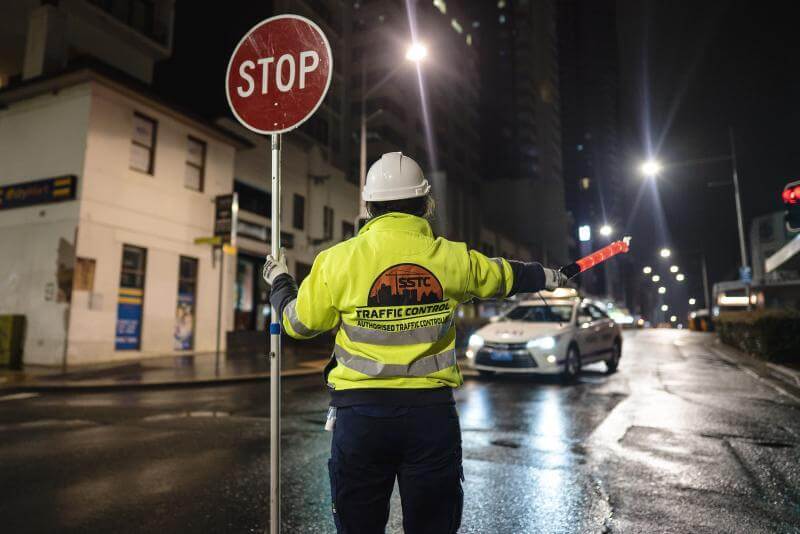 Accredited SSTC traffic controller holding STOP sign bat during night-time road closure in Sydney